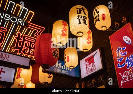 Close-up of Japanese lanterns hanging amidst neon signs in a night market, creating a warm and inviting atmosphere typical of Dotonbori. Osaka, Japan -14 June 2024 Stock Photo