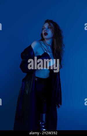 A fashionable red haired woman showcases her style in a captivating blue ambiance. Stock Photo