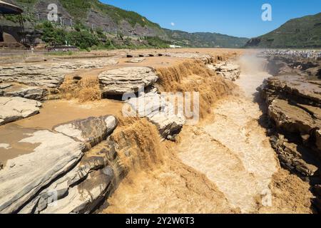 A stunning view of the Hukou Waterfall on the Yellow River in China, surrounded by rocky cliffs and a clear blue sky. Stock Photo