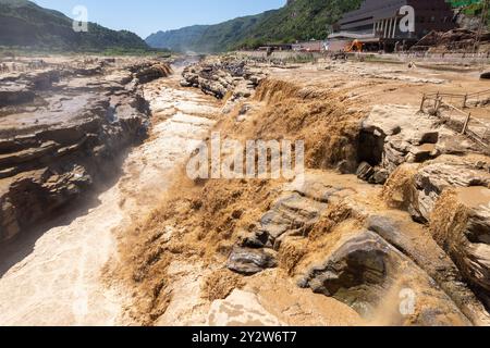 Hukou Waterfall on the Yellow River in China, showcasing the powerful flow and unique landscape, with tourists observing from viewing platforms. Stock Photo