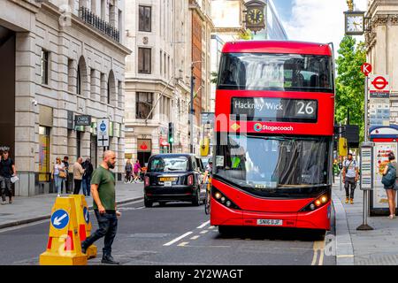 A No 26 red London double decker bus approaches a bus stop on  Poultry in The City Of London ,London, UK Stock Photo