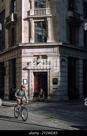 A cyclist passing by Bury Court building in London with a person sitting on the steps Stock Photo