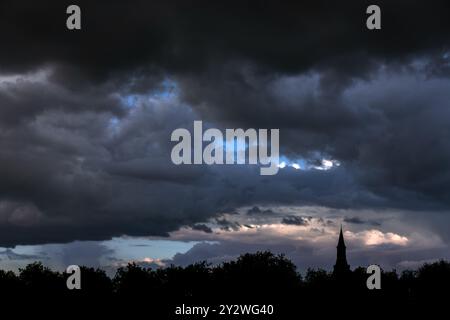 Treetops and church tower silhouetted against black nimbostratus cloud bringing rain in late summer Stock Photo