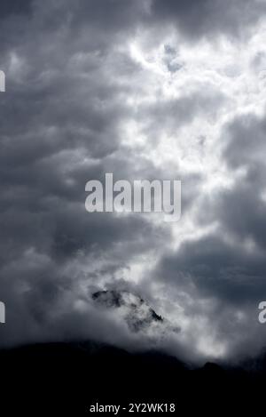 The sun glows behind clouds above a mountain peak in British Columbia, Canada Stock Photo