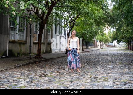 A young woman standing on a cobblestone street at Rainbow Row in South Carolina Stock Photo
