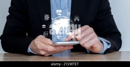 Businessman using a smartphone with digital icons representing global business and technology concepts. Stock Photo