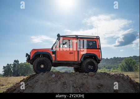 Detail of an old orange Land Rover Defender with external roll bars on top of mound in countryside Stock Photo