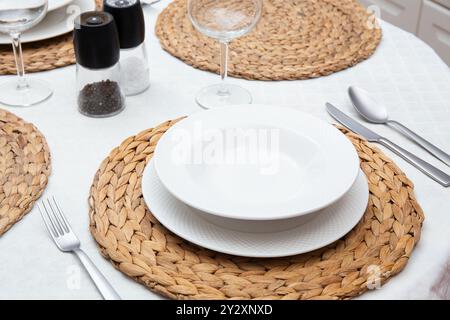 Set table in restaurant, featuring white plates, woven placemats, elegant cutlery, perfect for romantic date or fine dining experience Stock Photo