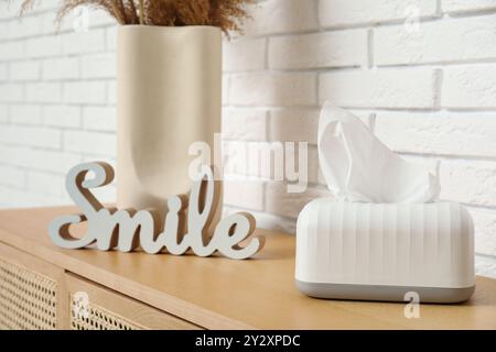 Tissue in ceramic holder and word SMILE on chest of drawers in living room. Closeup Stock Photo