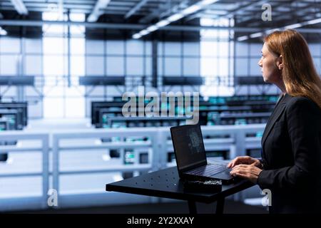 Technician programming in AI server farm housing advanced equipment used for machine learning training. Skilled admin running code on laptop to upgrade artificial intelligence systems Stock Photo
