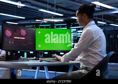 IT professional in server hub using mockup computer, trying to protect hardware from hacker. Cybersecurity expert in high tech data center workplace trying to fix security breach on green screen PC Stock Photo