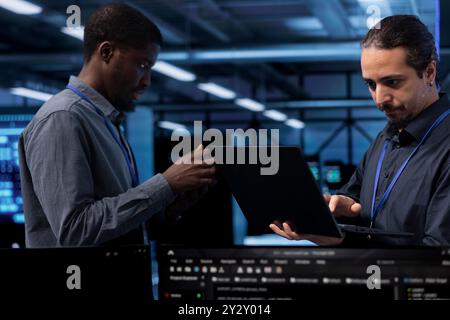 Programmers in data center running system diagnostic tests on laptop to fix problems. Employees deploying and error checking utilities on notebook to fix network issues performance Stock Photo