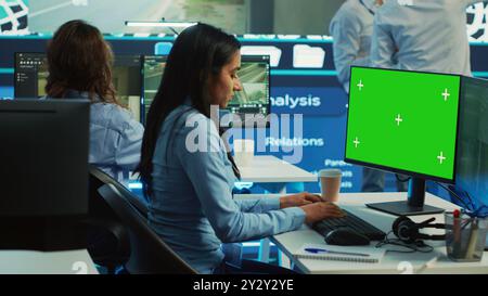 Indian employee follows order shipment next to a greenscreen on pc, communicating gps coordinates on satellite map for courier trying to avoid traffic. Cargo delivery agency. Camera A. Stock Photo