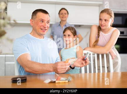 Father gives pocket money to children and wife in kitchen Stock Photo