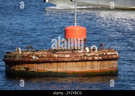 A weathered buoy with chains resting on a floating platform in a body of water. The buoy is orange and the platform shows signs of rust and algae grow Stock Photo