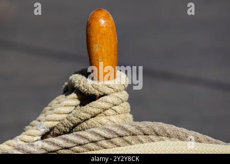 A close-up of a wooden handle on a rope, showcasing the texture of the rope and the polished wood. The background is blurred, emphasizing the details Stock Photo