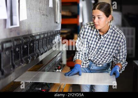 Young woman placing metal sheet on bending machine in workshop Stock Photo