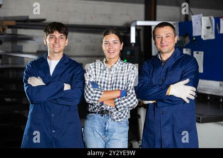 Portrait of two positive workers and girl student in the metalworking workshop of metallurgical plant Stock Photo