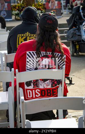A man sits at the day's program while wearing a red disobey shirt during the Missing and Murdered Indigenous Persons Day of Action at the capitol. Stock Photo