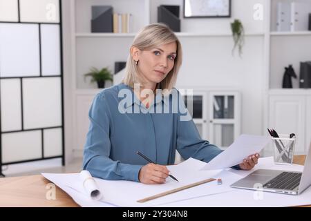 Architect making engineering drawing at table in office Stock Photo