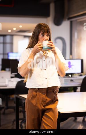 Taking break in modern office workspace, woman drinking coffee Stock Photo