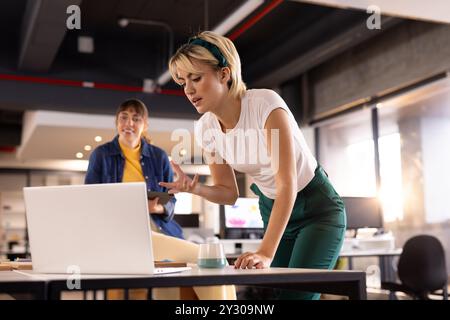 Collaborating on project details, multiracial women in modern office with laptop and tablet Stock Photo