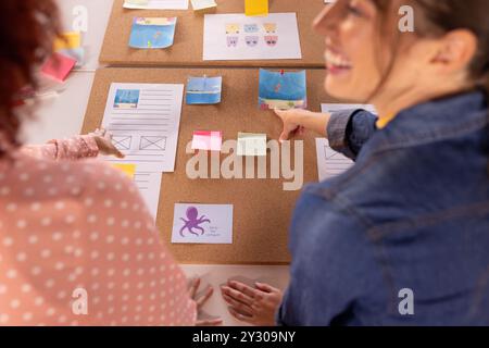 At office, collaborating on creative project, multiracial women using sticky notes and corkboard Stock Photo