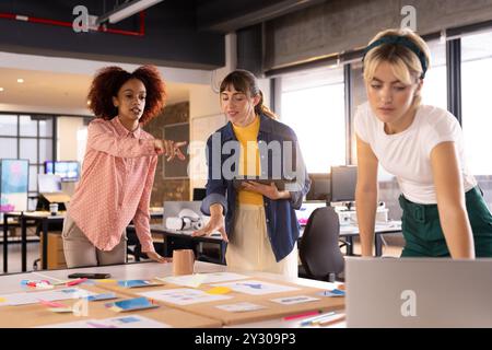Collaborating on creative writing project, three multiracial women discussing ideas in office Stock Photo