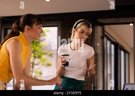 Discussing project ideas, two women collaborating in modern office with coffee cup Stock Photo