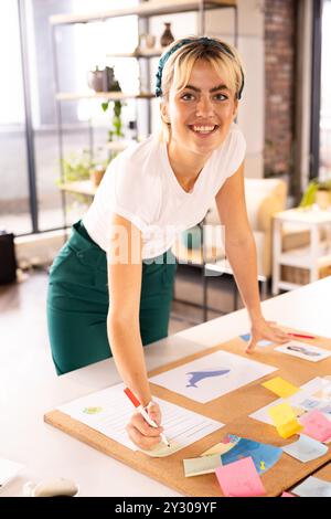 Smiling woman writing on sticky notes, planning creative business ideas in office Stock Photo