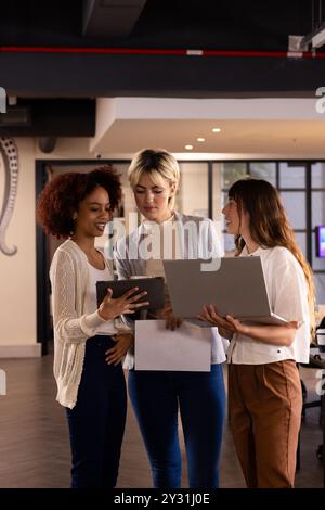 Collaborating in office, three multiracial women discussing project using laptop and tablet Stock Photo