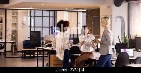 Discussing project ideas, three multiracial women holding coffee cups in modern office Stock Photo
