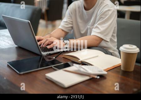 A cropped image of a man working remotely from a coffee shop, working on his laptop, typing on the laptop keyboard. people and technology concepts Stock Photo