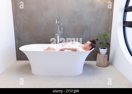 At home, Relaxing in bathtub, young woman enjoying bubble bath in modern bathroom Stock Photo