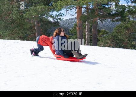 Boy pushing his mother on a sled in the snow Stock Photo