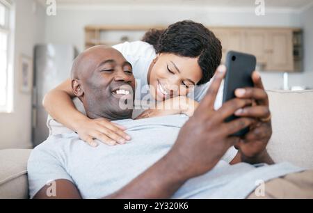 Black couple, home and smile with smartphone on couch with hug for social media post and funny videos. People, relationship and happy or laughing on Stock Photo