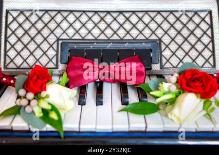A red bow tie and a matching boutonniere rest on the keys of a vintage piano, illuminated by warm light. Stock Photo
