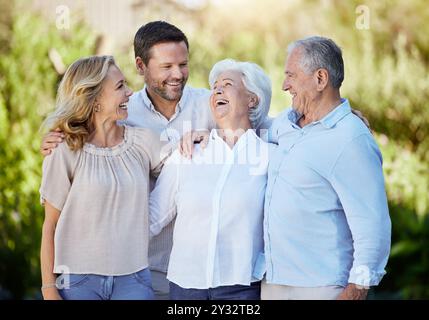 Happy, love and big family hug laughing in park for holiday, travel or weekend trip. Nature, smile and couple embrace elderly parents for vacation Stock Photo