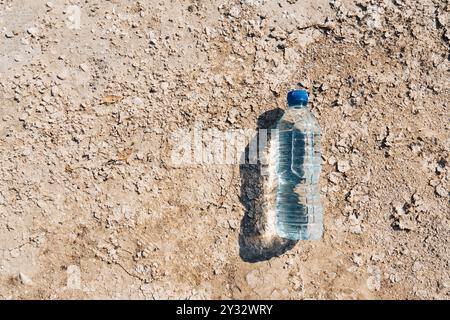 A bottle of water lies on the bottom of a dry lake on a sunny summer day. Concept of the problem of climate change Stock Photo