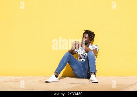 african man sitting at floor against yellow wall Stock Photo
