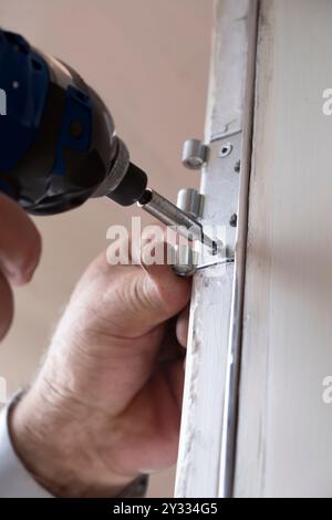 Handyman with automatic screwdriver turns a screw in a hinge of a window in an older house to be renovated Stock Photo