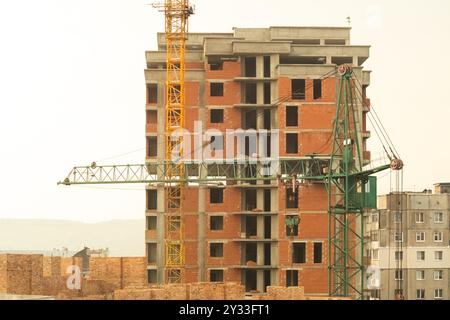 A mid-rise brick building under construction with two cranes working on-site. The structure is still in the early stages, showing exposed brick and em Stock Photo