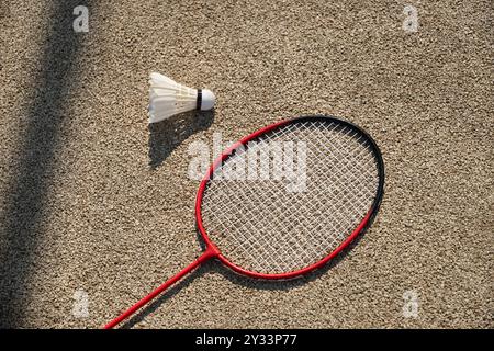 White badminton feather shuttlecock and badminton racket on beige floor sport badminton court in sunny shadow. Summer game outdoors. Close up. Stock Photo