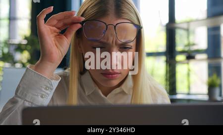 Caucasian woman businesswoman business girl take off glasses looking at laptop screen confused blurry vision after computer overwork in office Stock Photo