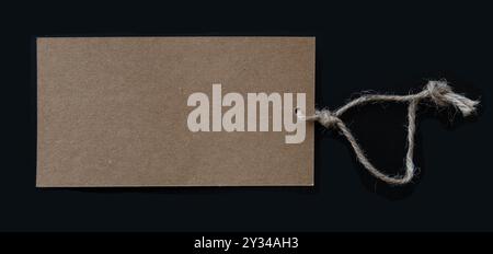 Blank brown tag with rustic thread string isolated on black background. Copy space. Stock Photo