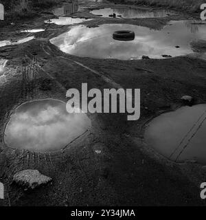 Dirt road in huge puddles and a car tire. Black and white photography Stock Photo