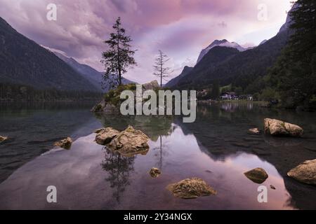 Hintersee with rocks and trees in the foreground, surrounded by mountains after sunset with dramatic cloudy sky, Ramsau, Berchtesgaden National Park, Stock Photo