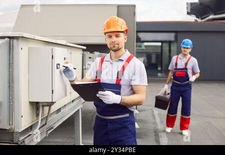 Focused Worker Inspecting HVAC System on Roof Stock Photo