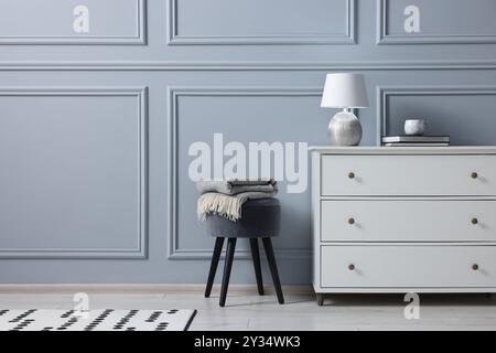 Stylish interior with stool and chest of drawers near light grey wall, space for text Stock Photo