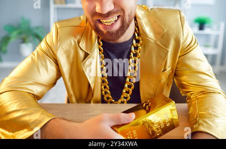 Close up cropped photo of happy funny young man holding gold bar sitting celebrating success. Stock Photo